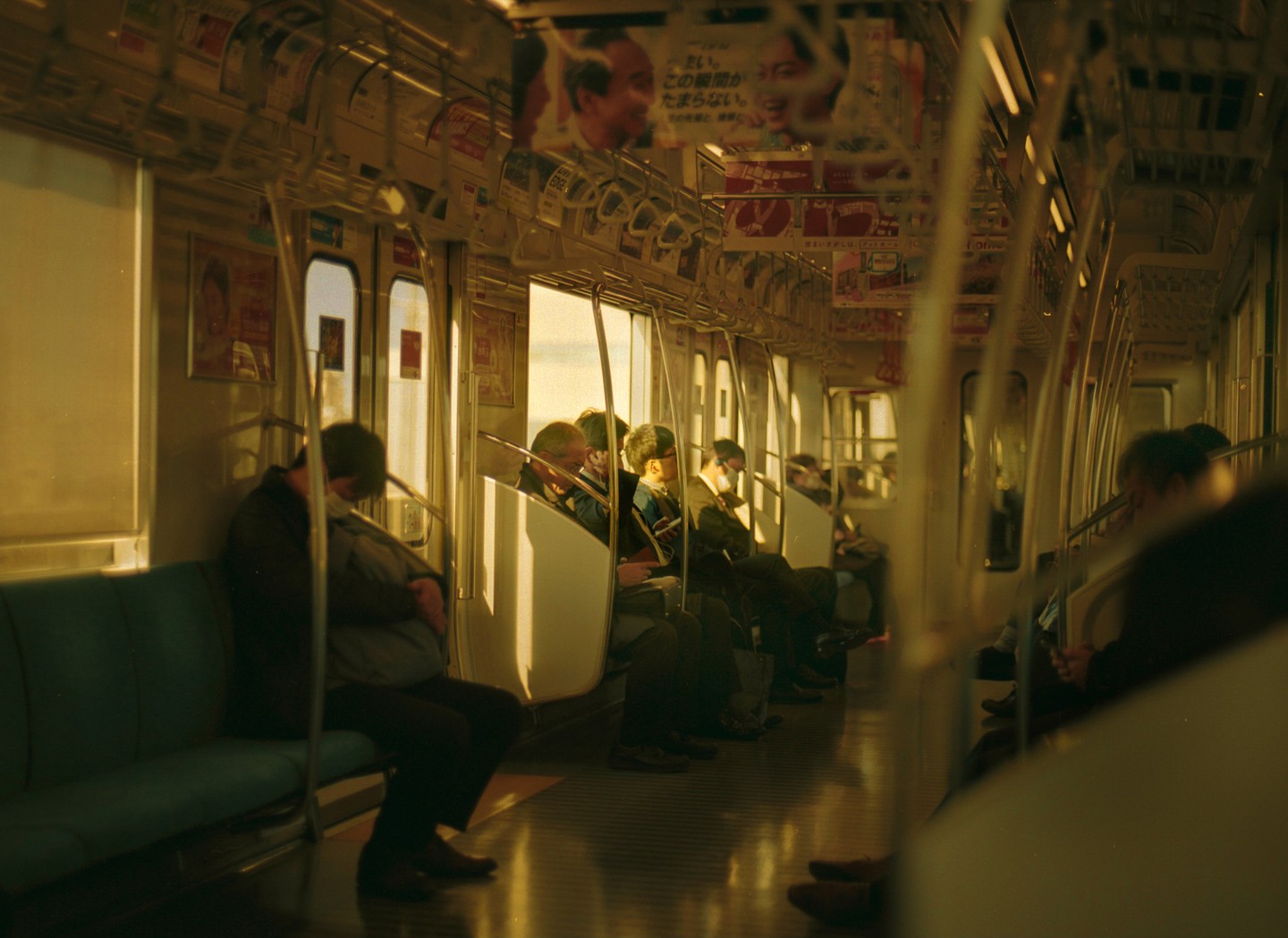 People are sitting and standing inside a subway car with warm light coming through the windows.