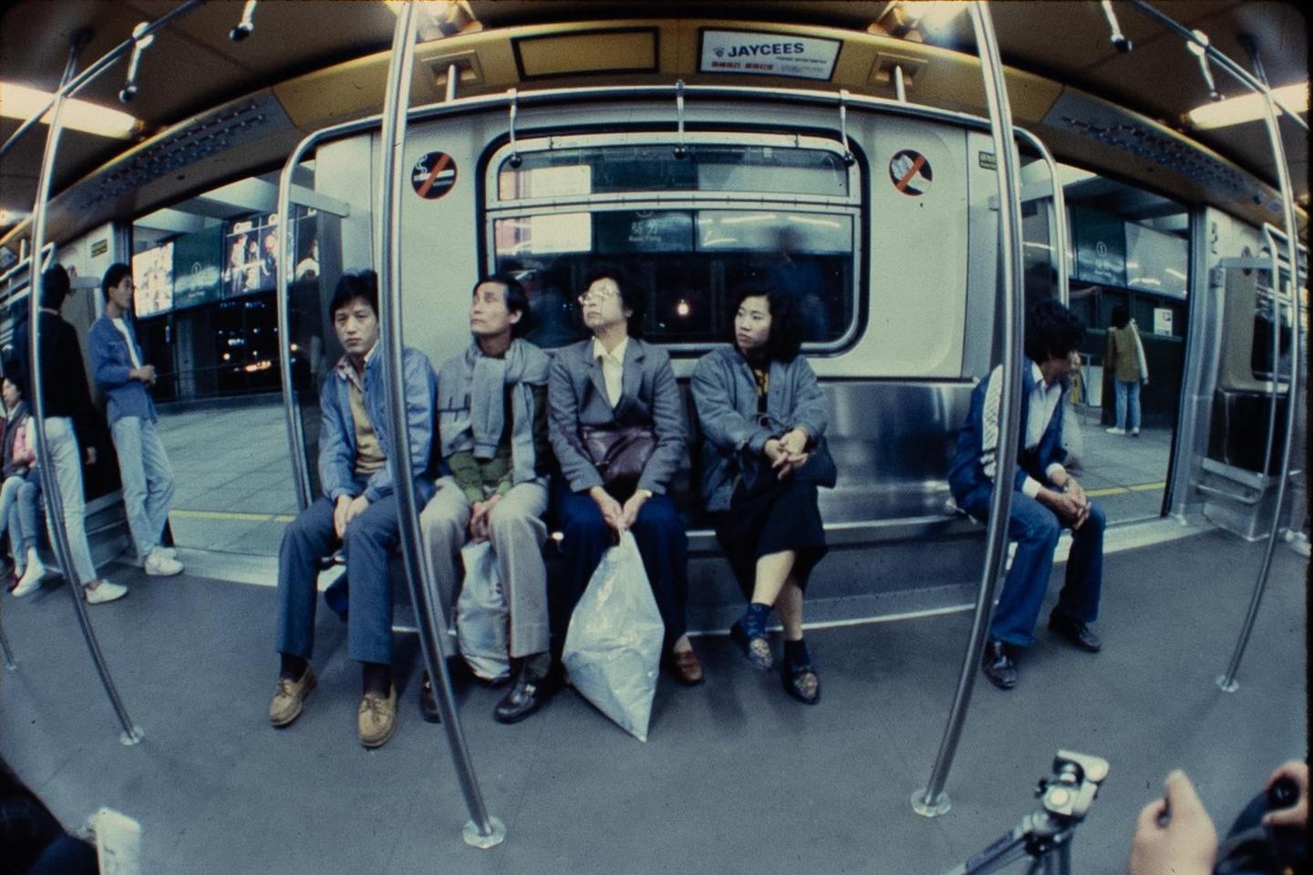 A group of people are sitting on a subway train with a fisheye perspective.
