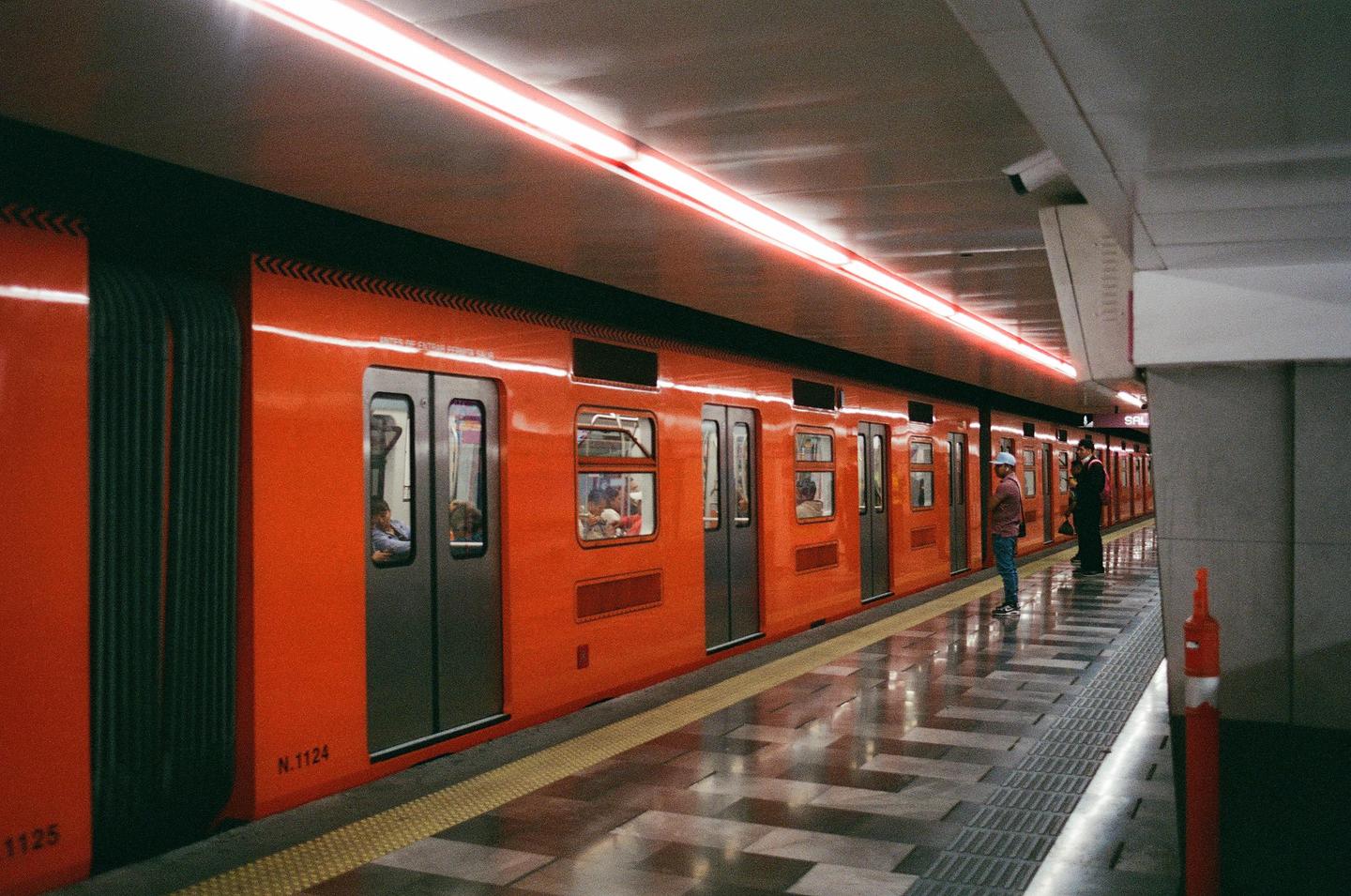 An orange subway train is stopped at a station platform with people waiting and sitting inside.