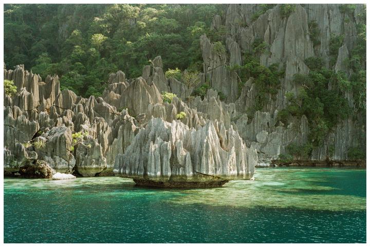 Jagged limestone karsts covered with lush green foliage rise from clear turquoise water.