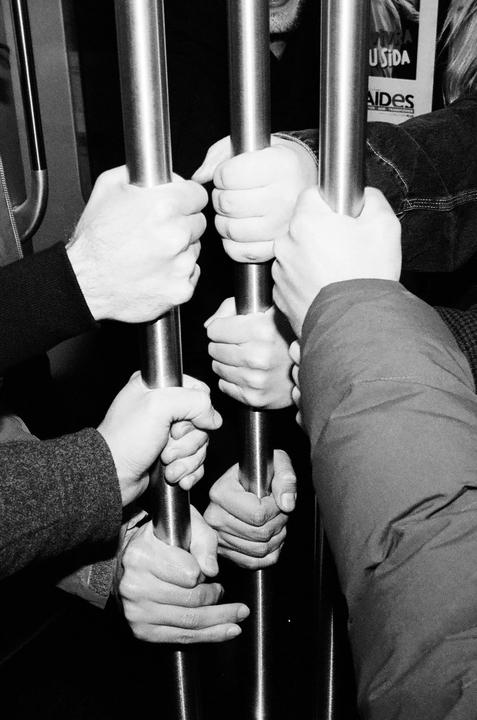 Multiple hands are gripping metal poles in a black and white photograph.