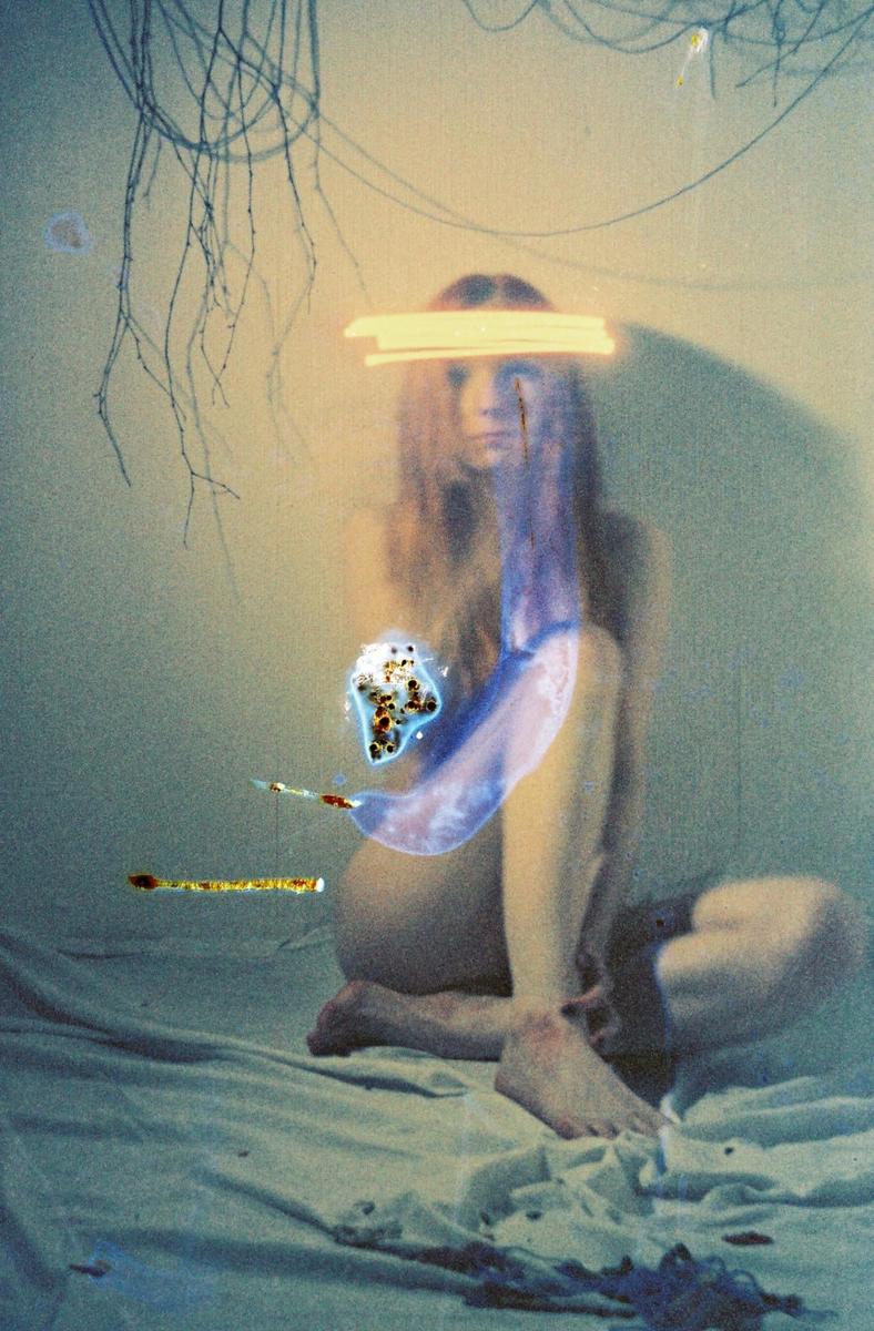 A woman with long hair sits on a bed with light streaks across her face and body.