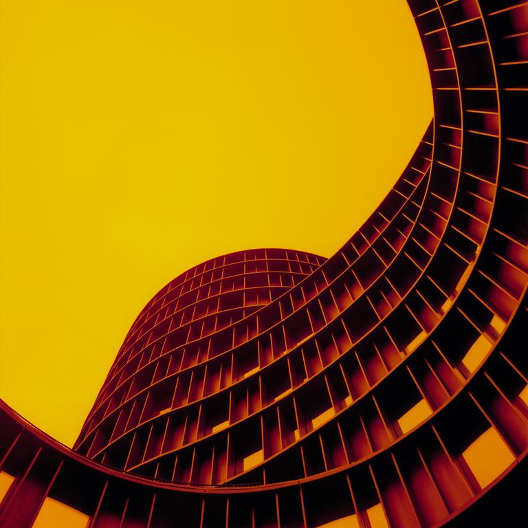 A low-angle view shows the curved facade of a building against a bright yellow sky.