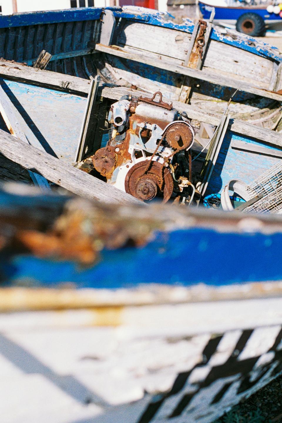 A rusty engine sits inside a weathered blue and white boat.