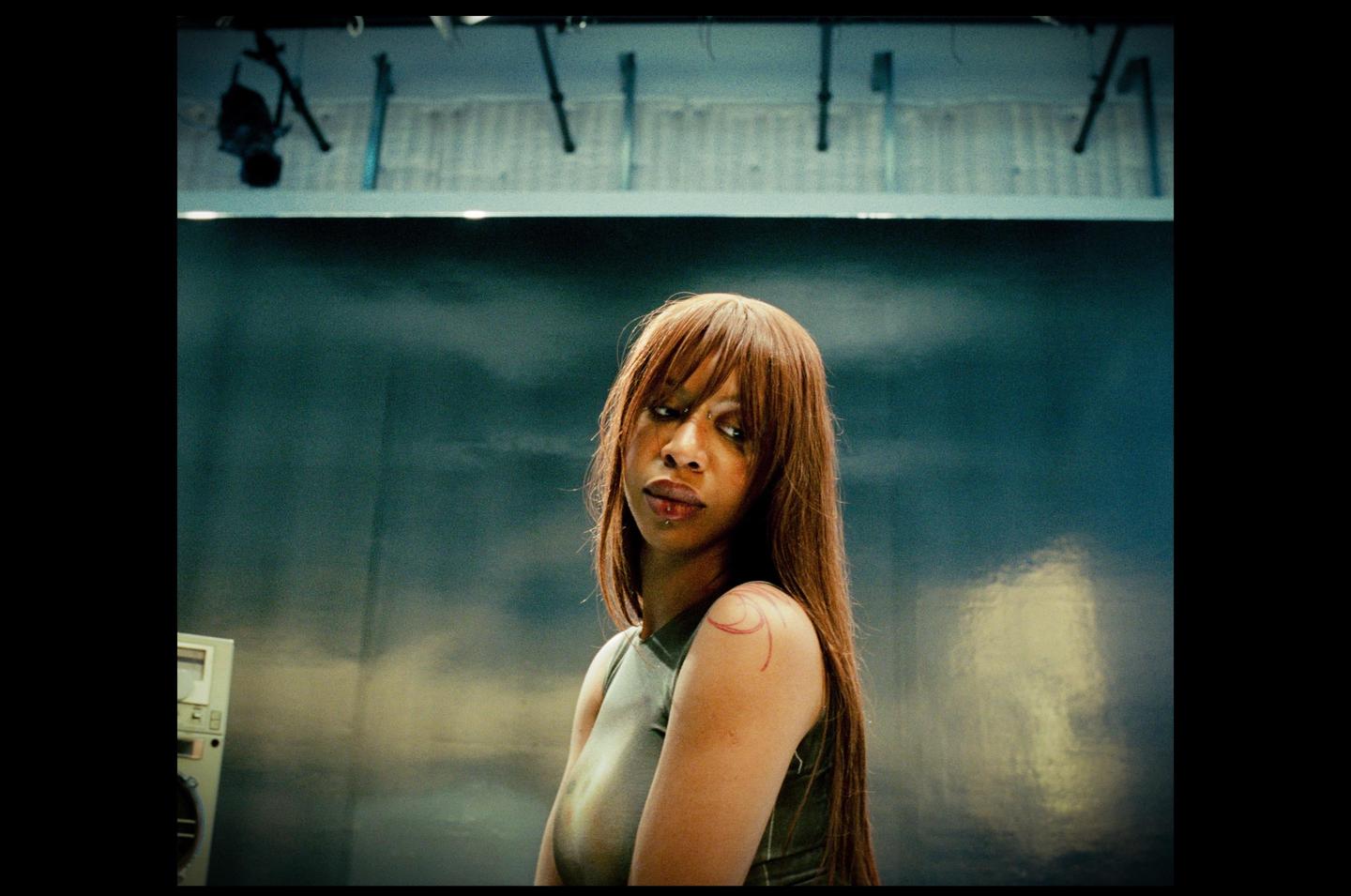 A woman with long hair and a tattoo on her shoulder looks to the side.