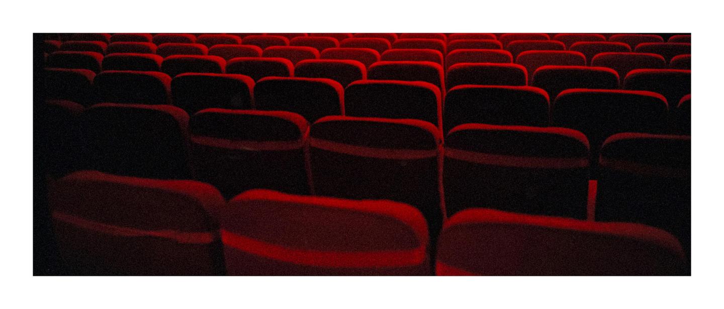 Rows of empty red seats are visible in a dark theater.