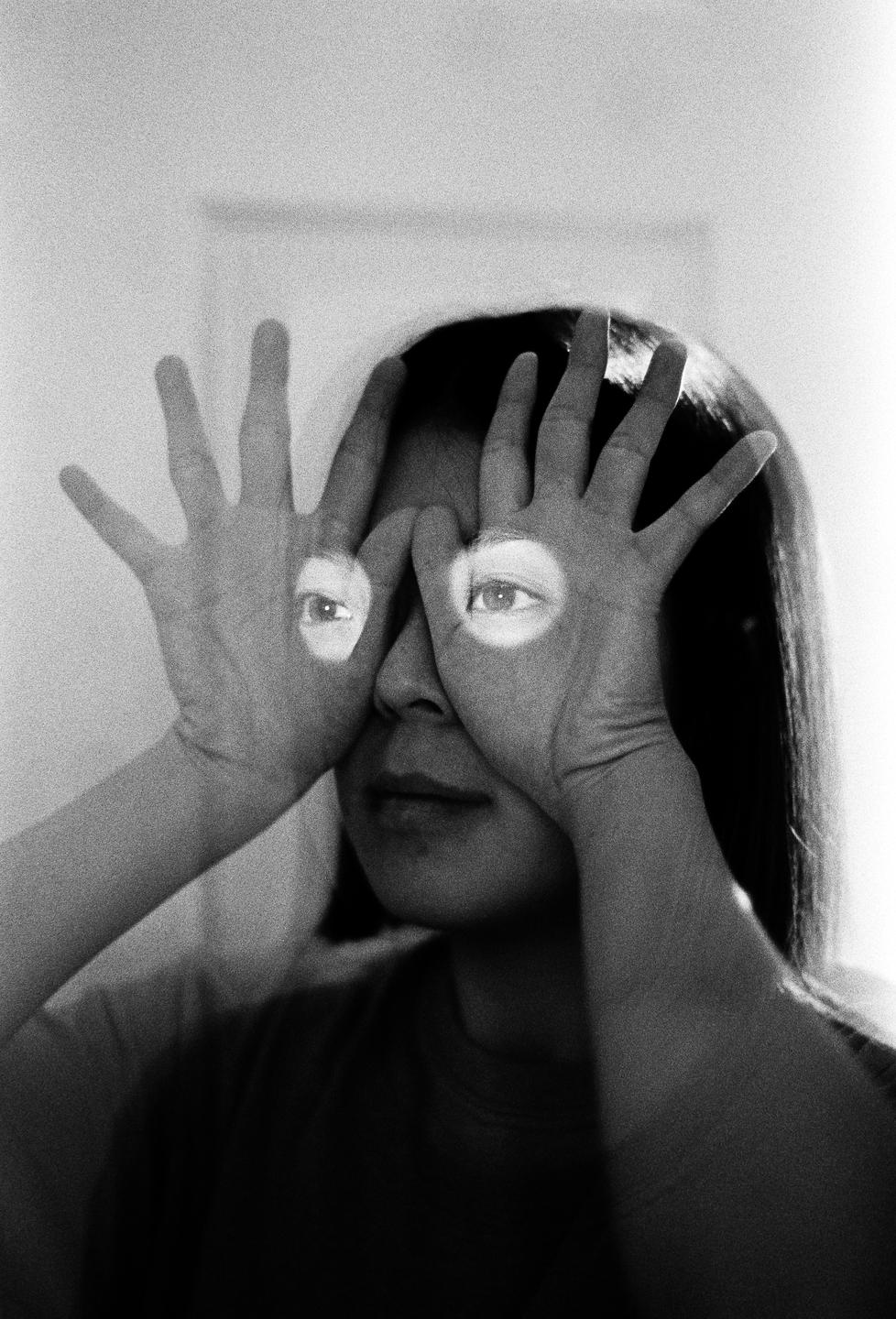 A woman holds her hands over her face with eyes projected onto her palms.