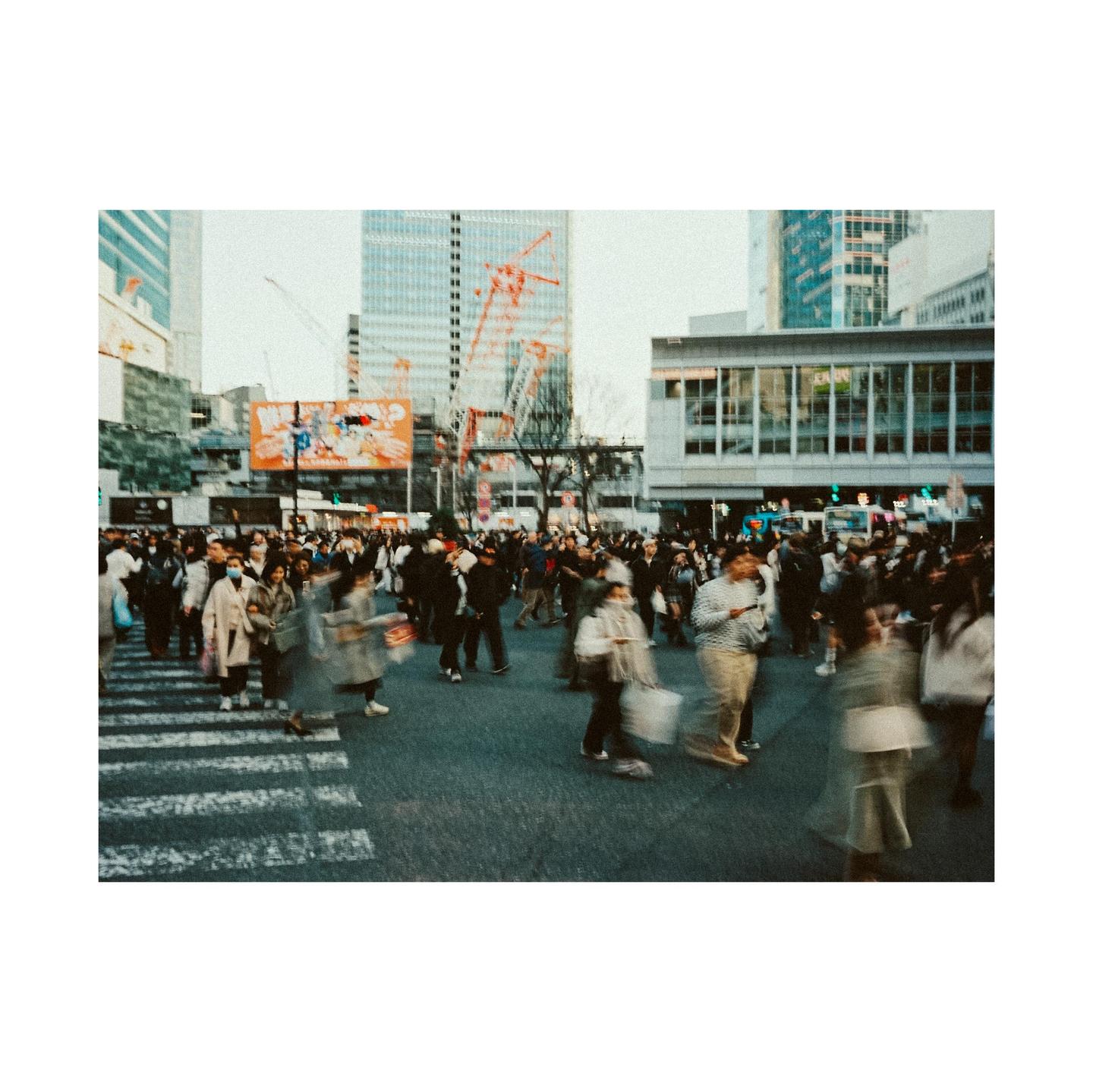 A large crowd of people crosses a street in a city with tall buildings in the background.