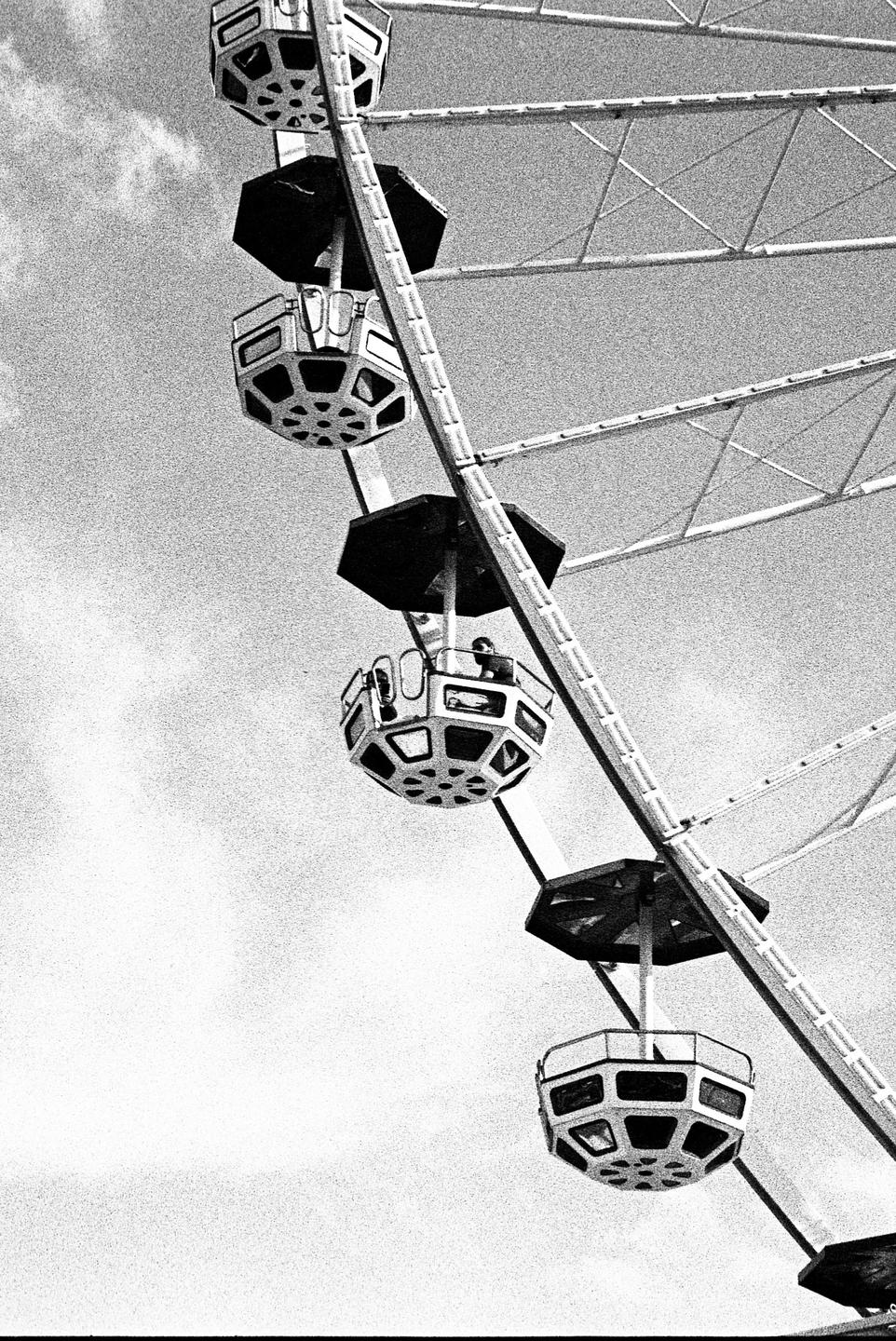 A ferris wheel with several gondolas is captured against a cloudy sky.