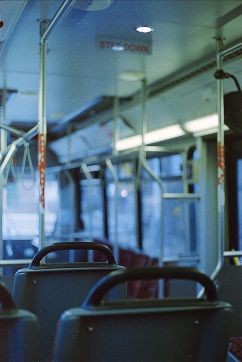 The interior of a bus is visible from the perspective of a passenger seat, with a "STEP DOWN" sign on the ceiling.