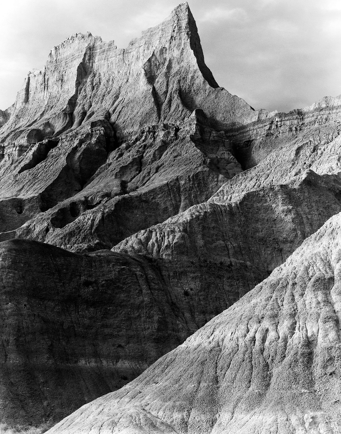 A black and white landscape shows a jagged mountain peak and eroded hills.