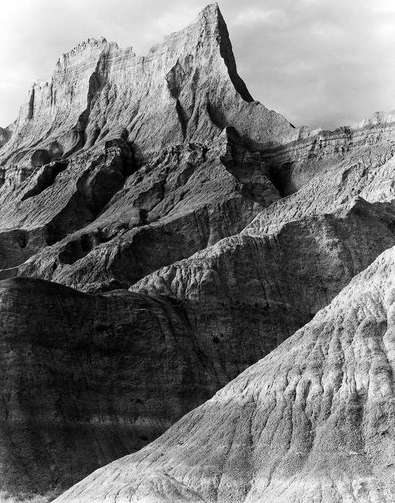 A black and white landscape shows a jagged mountain peak and eroded hills.