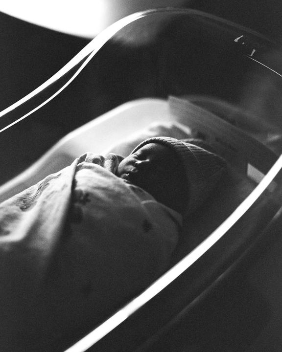 A newborn baby sleeps swaddled in a bassinet.