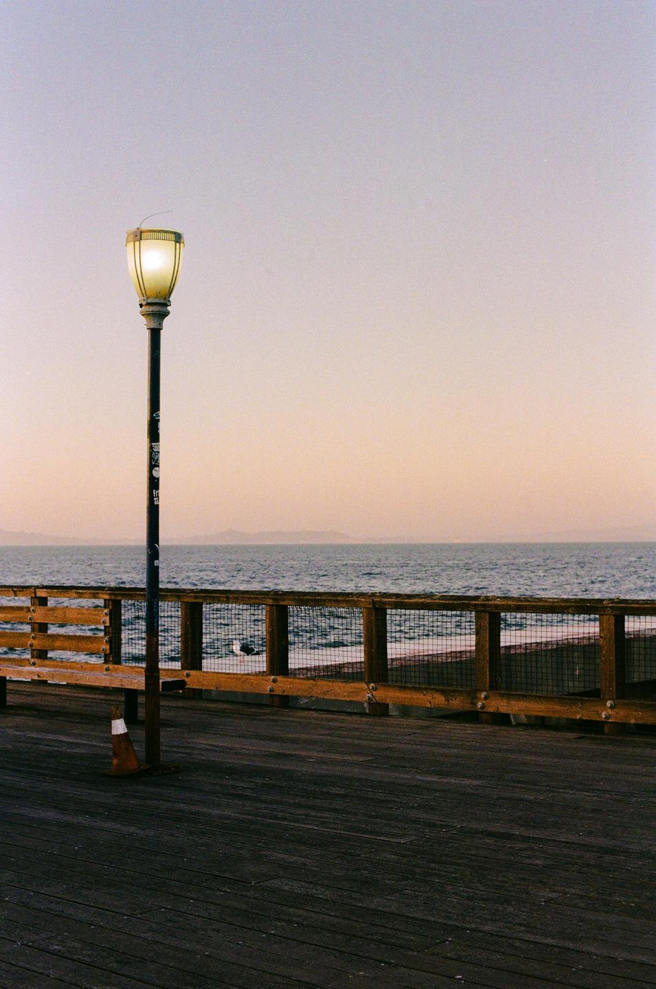 A street light illuminates a pier overlooking the ocean at dusk.