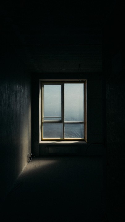 Sunlight streams through a window covered with plastic sheeting into a dark, empty room.