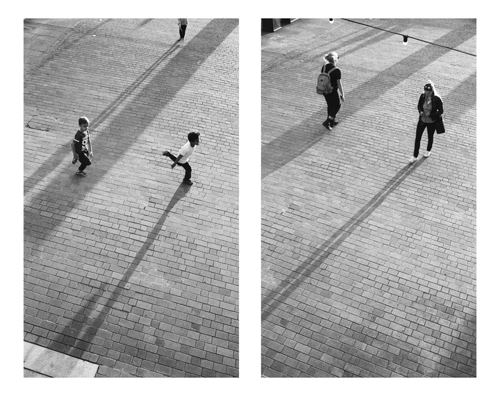 Two children and two women walk on a brick plaza, casting long shadows.