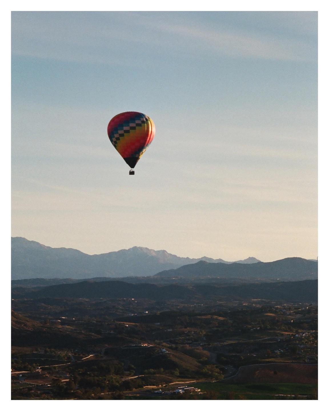 A colorful hot air balloon floats above a valley with mountains in the distance.