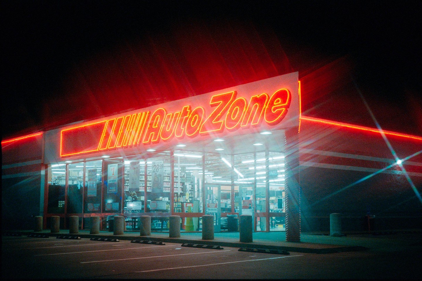 An AutoZone store with bright red neon lighting illuminates a dark parking lot at night.
