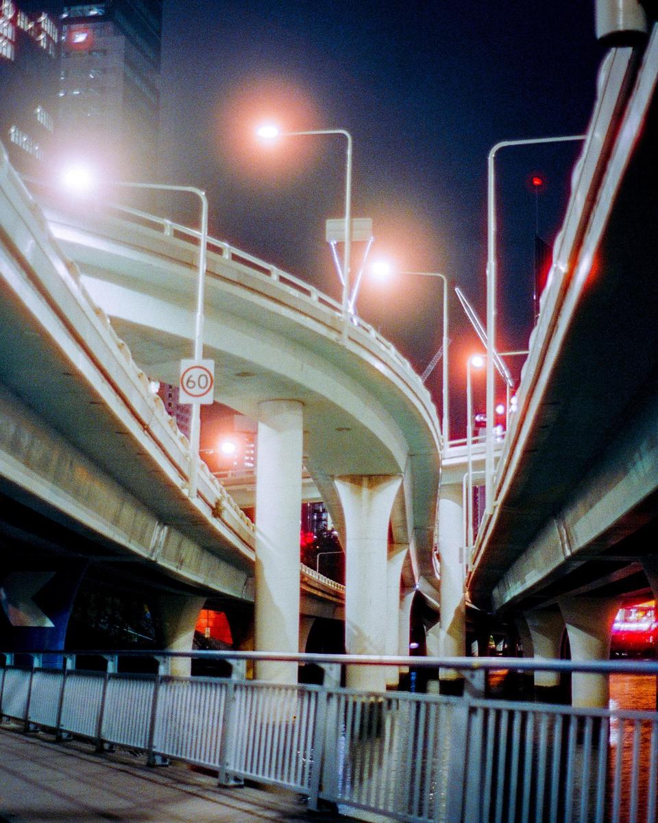 Multiple elevated highways with streetlights curve through the night, with a railing in the foreground.