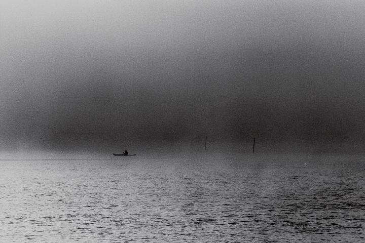 A person in a kayak is on the water in the fog.