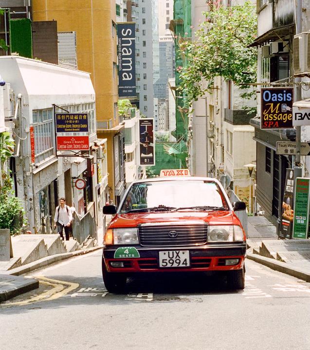 A red taxi is parked on a narrow street lined with buildings and signs.