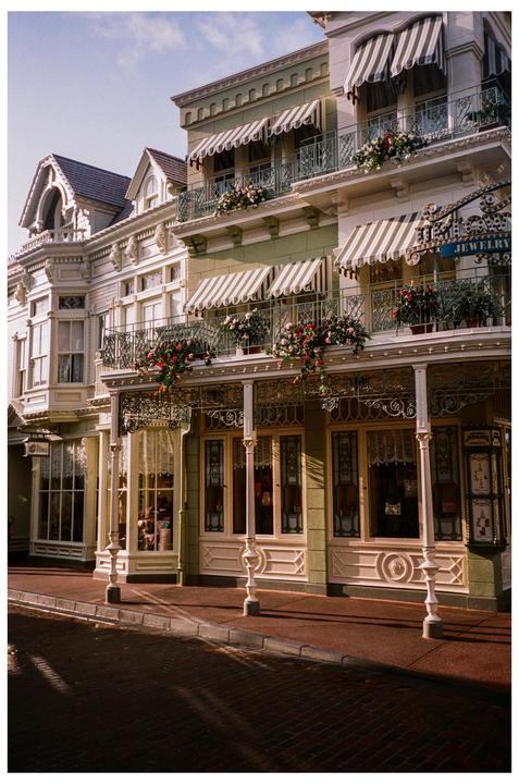 A row of ornate buildings with striped awnings and flower boxes line a brick street.