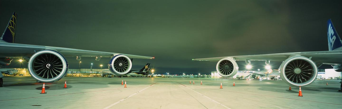 Two airplanes are parked on an airport tarmac at night, with their engines and wings prominently displayed.