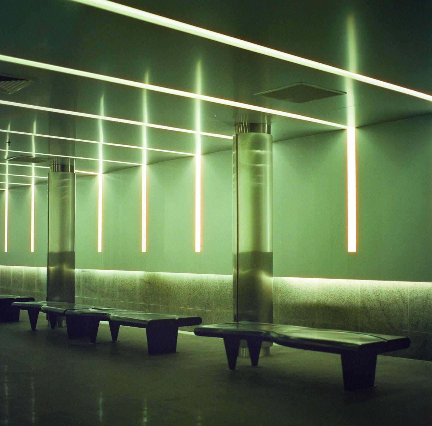 A row of benches sits in a room with green walls and linear lights on the ceiling and walls.