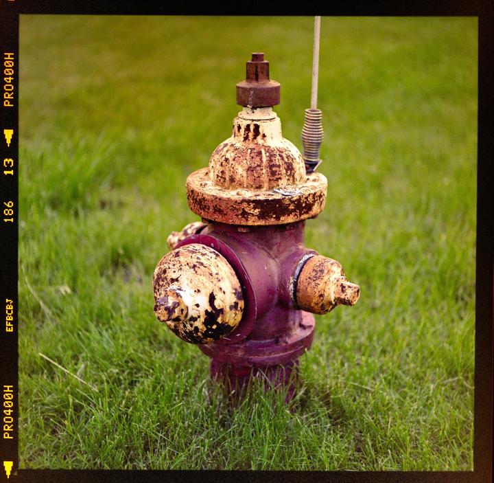 A rusty fire hydrant stands in a field of green grass.