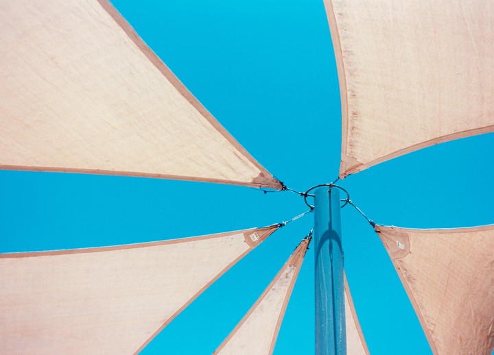 A blue pole is surrounded by beige fabric triangles against a bright blue sky.