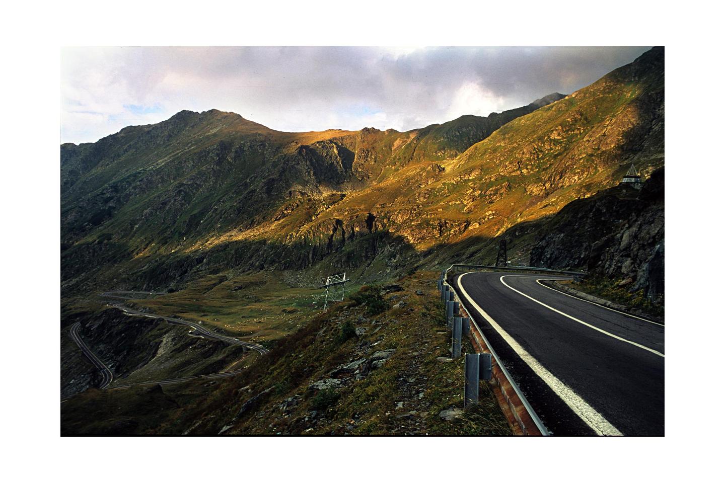 A winding road curves through a mountainous landscape under a cloudy sky.