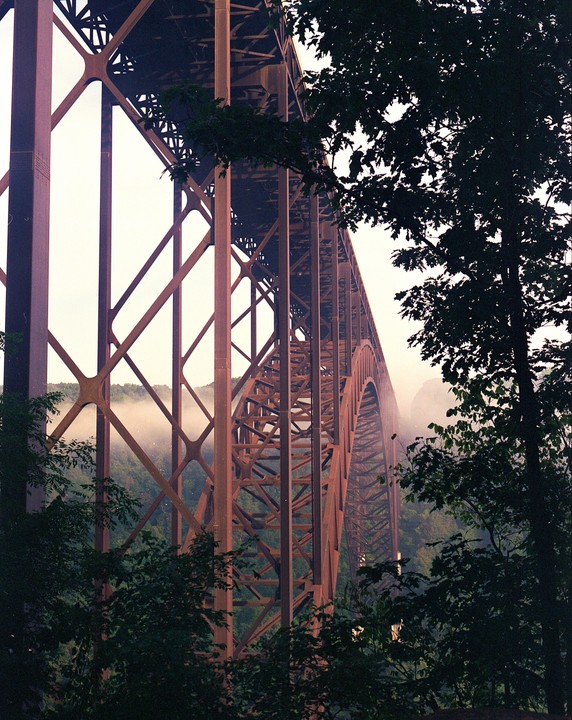A large metal bridge spans a valley with trees and fog.