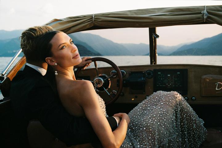 A couple sits in a boat on a lake with mountains in the background.