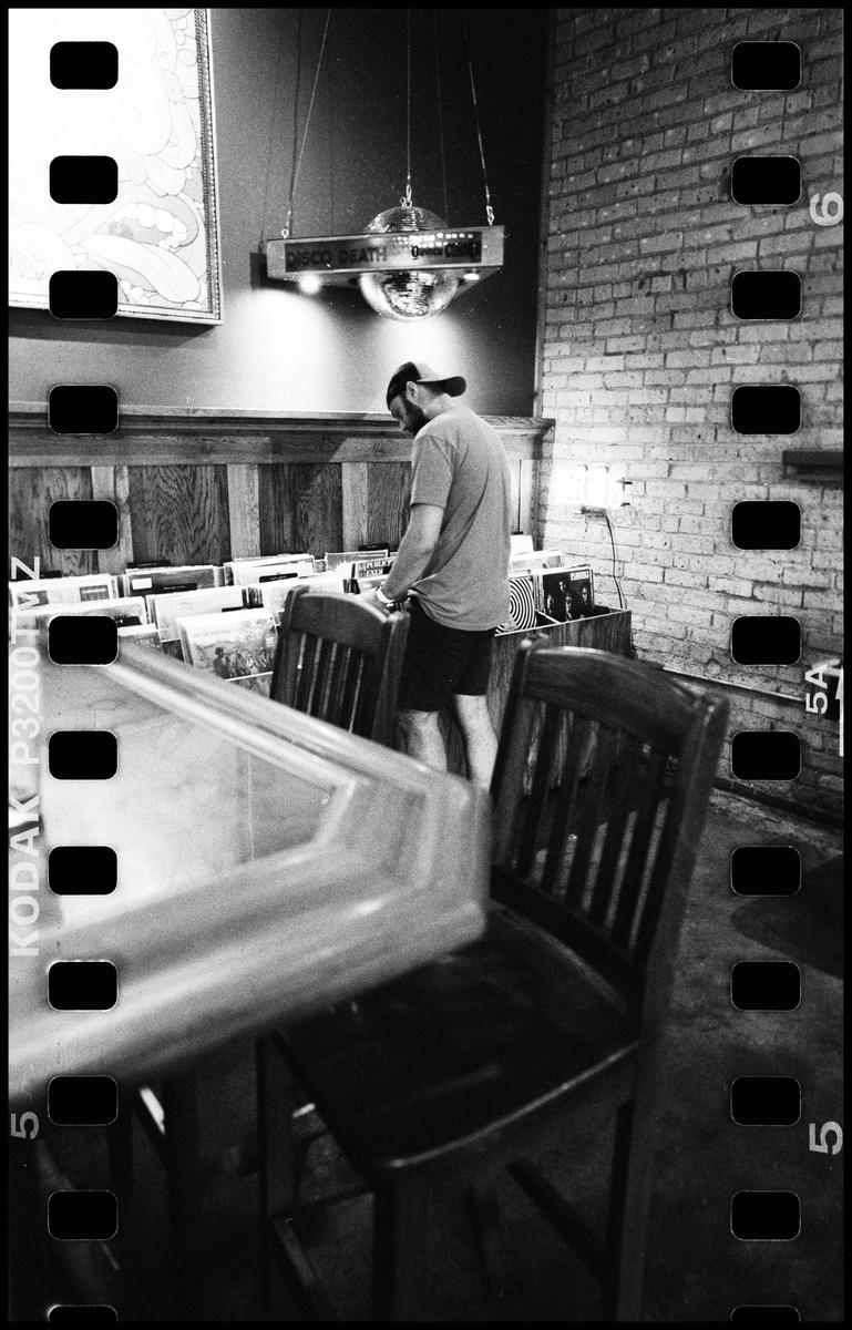 A man stands in a record store, looking through records, with a disco ball hanging above him.