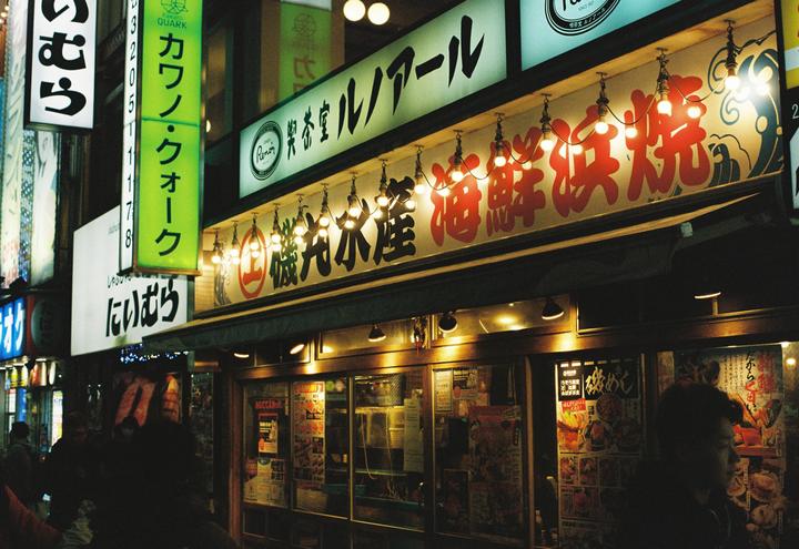 A street at night is illuminated by the neon signs of several businesses.