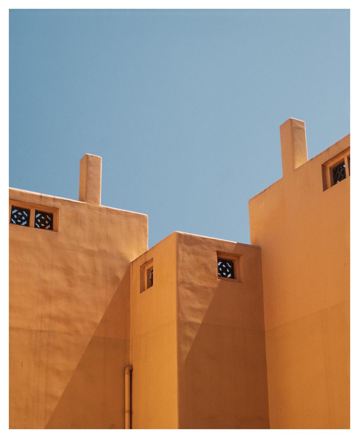 A building with orange walls and small windows is shown against a clear blue sky.