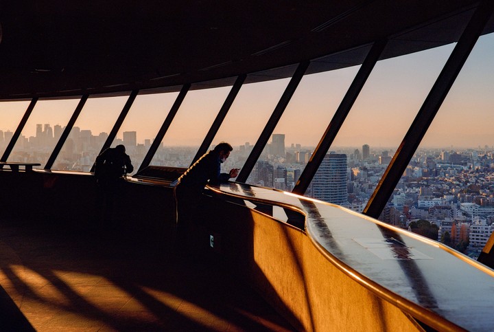 Two men look out over a city skyline from an observation deck at sunset.