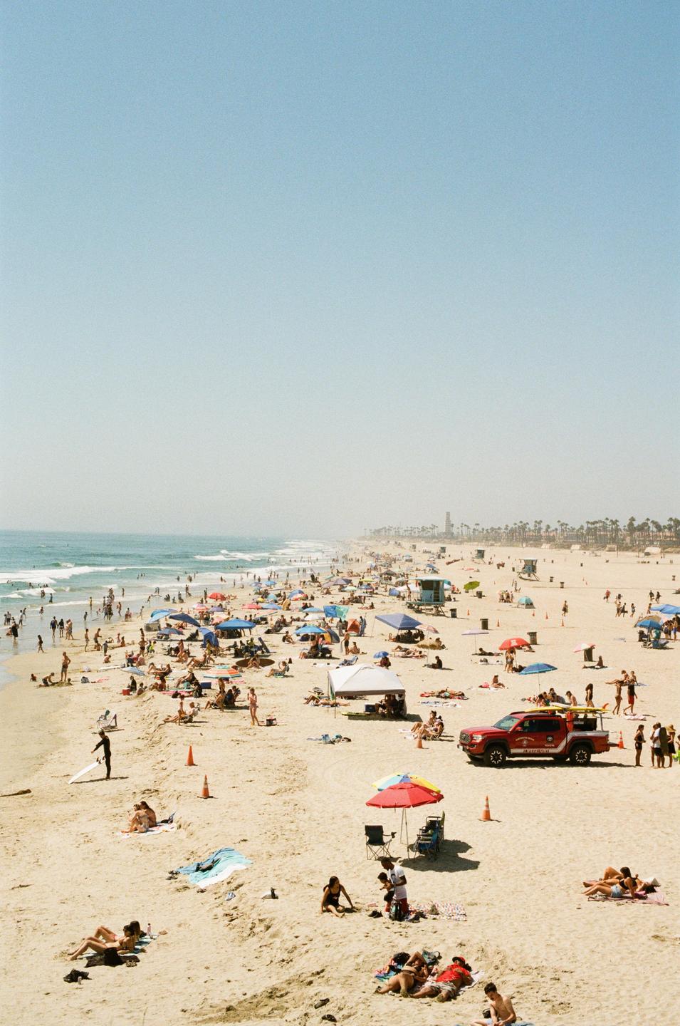 A crowded beach is filled with people swimming, sunbathing, and relaxing under colorful umbrellas and tents.