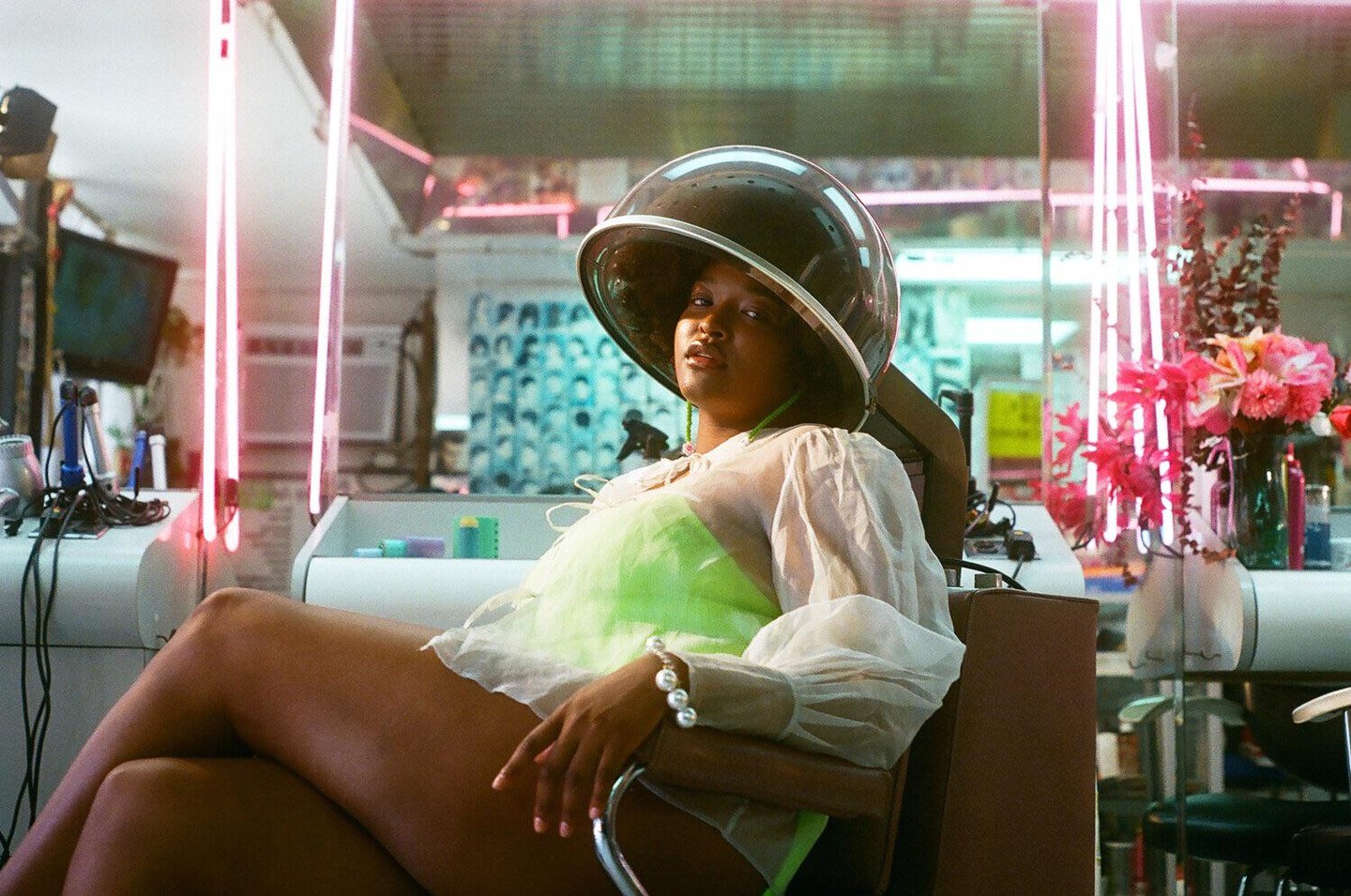 A woman sits under a hair dryer in a salon with neon lights.
