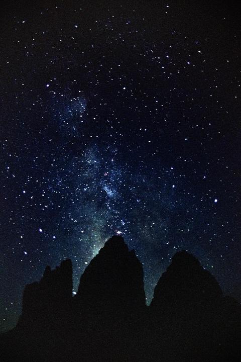 The Milky Way is visible above the dark silhouettes of mountain peaks.