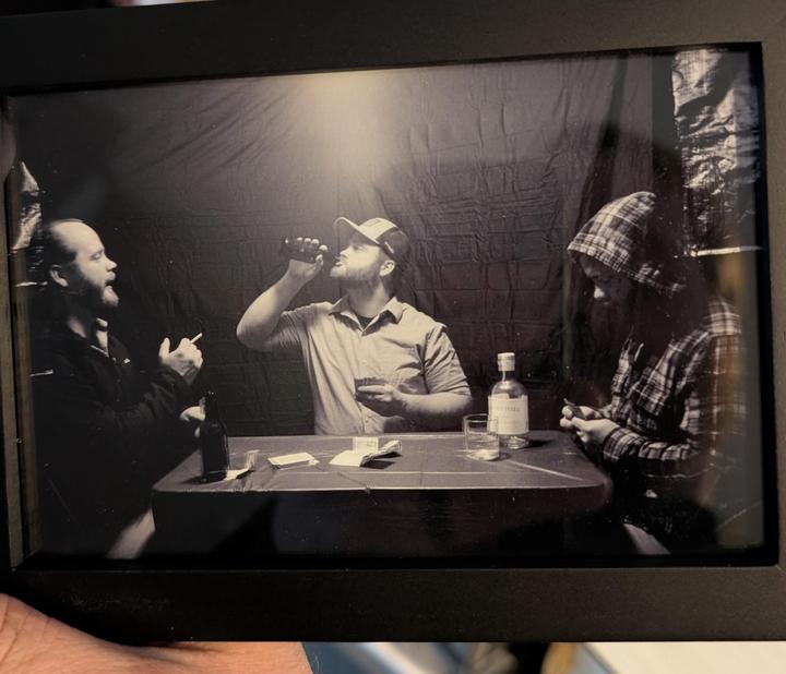 Three men are sitting around a table with drinks and playing cards.