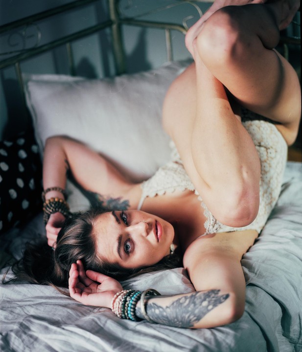 A woman with tattoos and bracelets is lying on a bed with her legs bent.