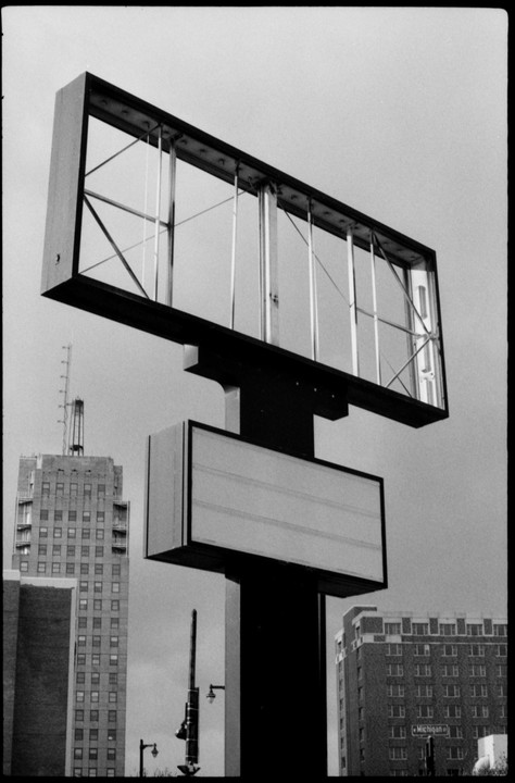 A tall, empty billboard sign stands in front of several buildings in a city.