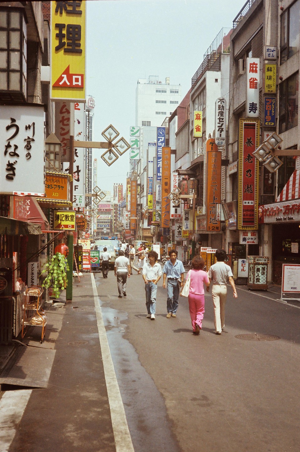 People walk along a narrow street lined with buildings and signs in Tokyo.