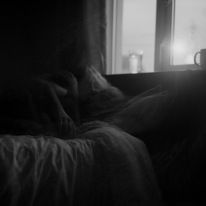 A person is lying in bed next to a window with a glass and a mug on the sill.