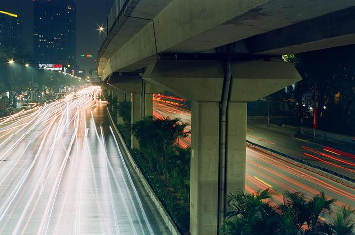 Light trails from vehicles on a multi-lane road at night are visible under an overpass.