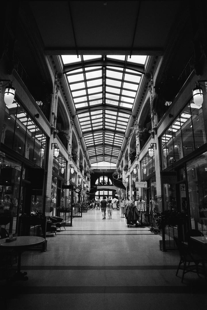 Two people walk down a long, narrow shopping arcade with a glass ceiling.