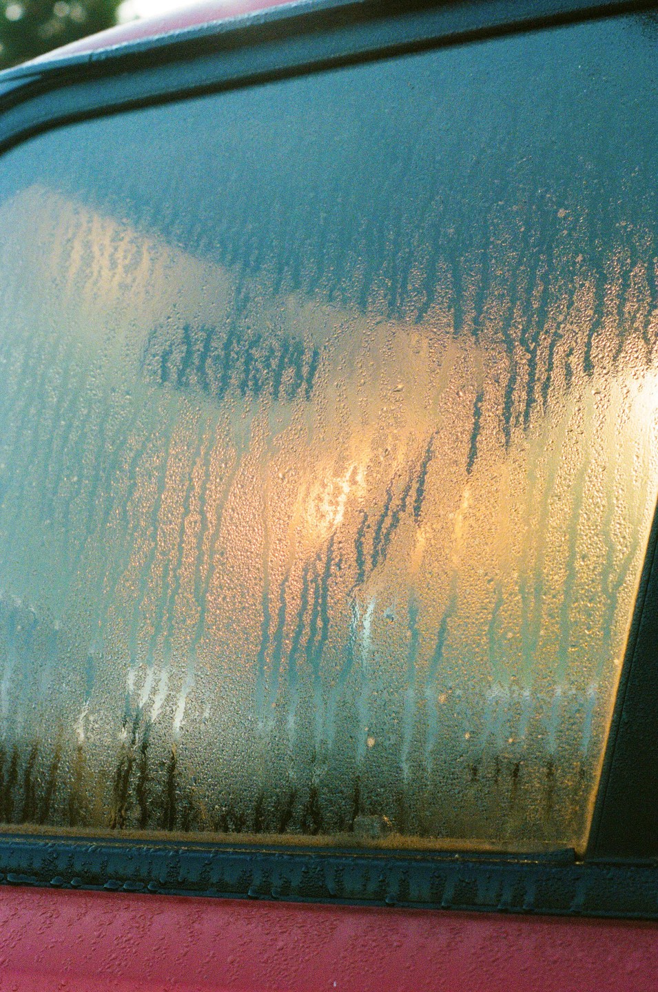 The morning sun shines through a dew-covered car window.