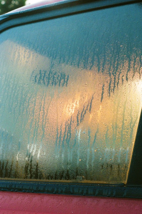 The morning sun shines through a dew-covered car window.