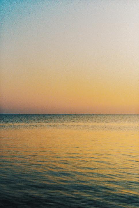 The sun sets over a calm body of water with a distant horizon.